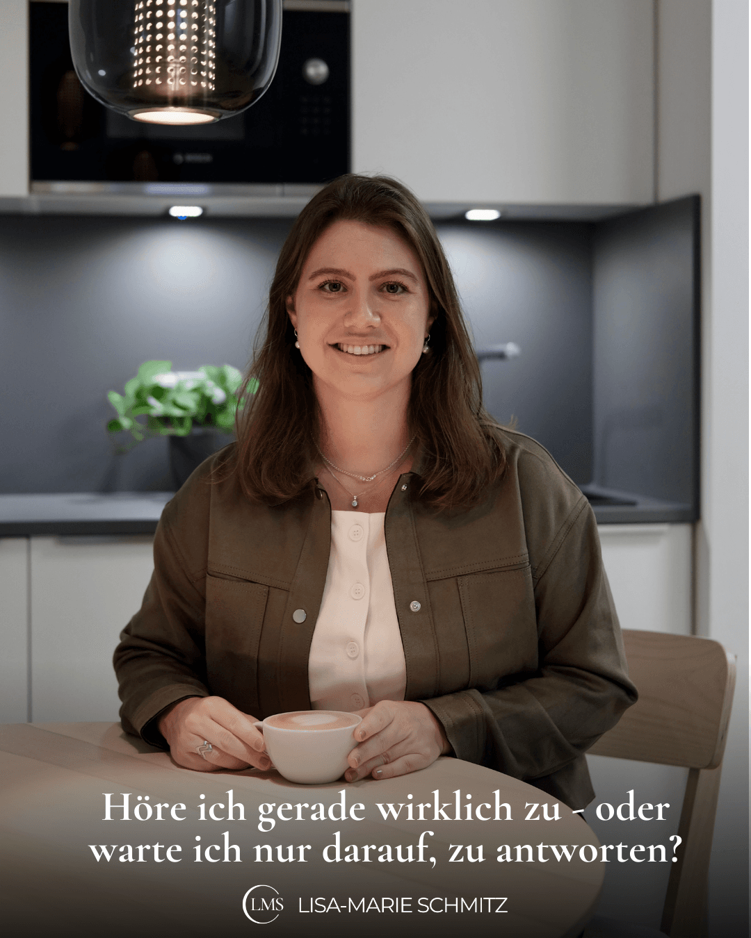 Das Bild zeigt Lisa-Marie, wie sie in einer dunkelgrünen Jacke in offener Haltung am Tisch sitzt, in die Kamera blickt, einen Kaffee in der Hand hält. Auf dem Bild steht die Frage: Höre ich gerade wirklich zu - oder warte ich nur darauf, zu antworten?