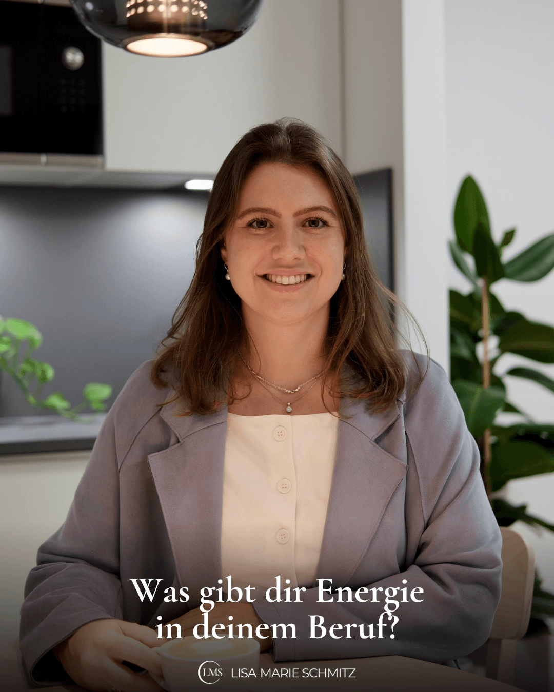 Lisa-Marie sitzt in einem hellblauen Blazer mit einer Kaffeetasse in der Hand an einem Tisch in einer modernen Küche und lächelt in die Kamera, auf dem Bild steht die Frage: Was gibt dir Energie in deinem Beruf?