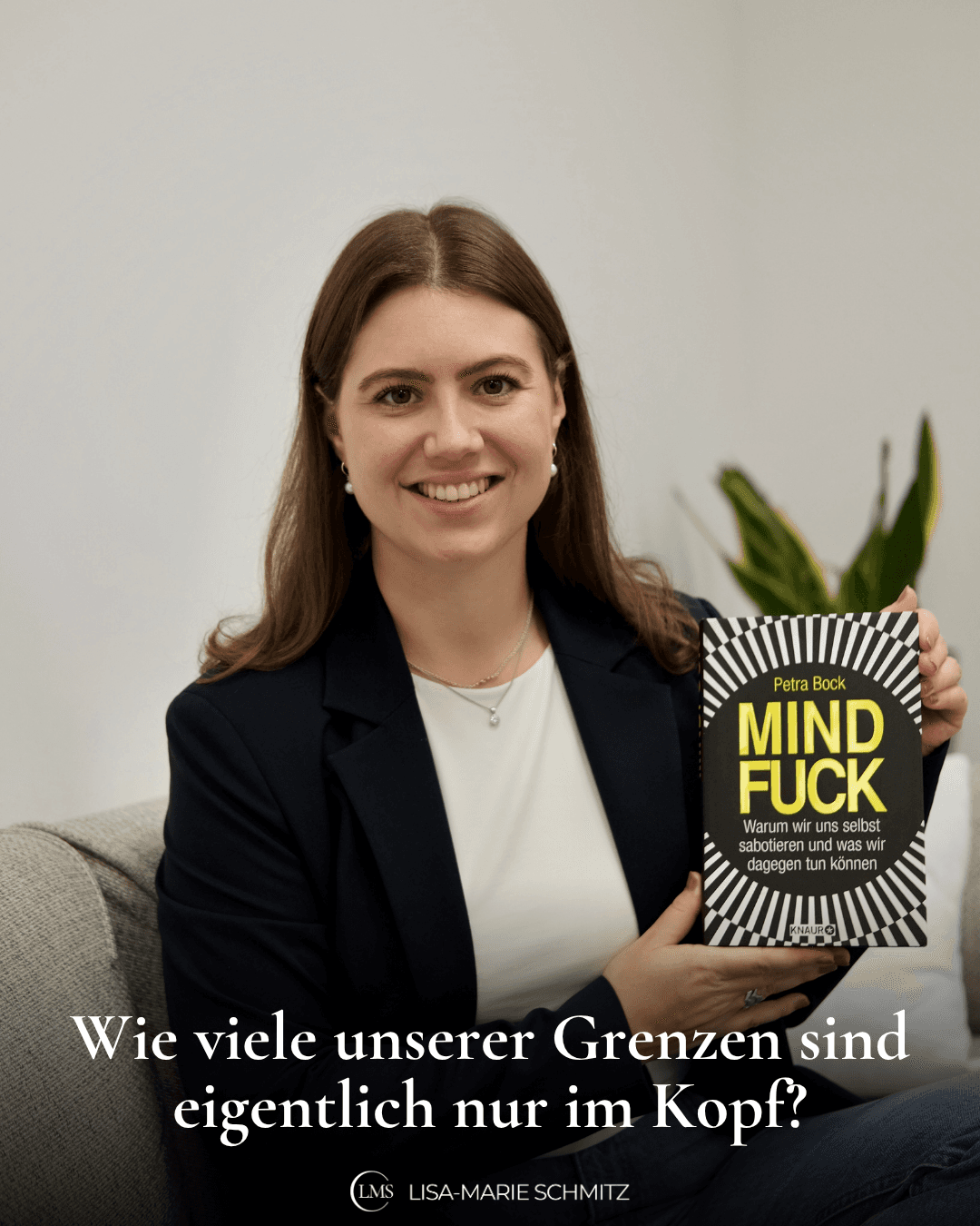 Lisa-Marie sitzt in einem dunkelblauen Blazer auf einer Couch, lächelt in die Kamera und zeigt ein Buch in ihren Händen von Dr. Petra Bock mit dem Titel 'Warum wir uns selbst sabotieren und was wir dagegen tun können' und auf dem Bild steht die Frage: Wie viele unserer Grenzen sind eigentlich nur im Kopf?