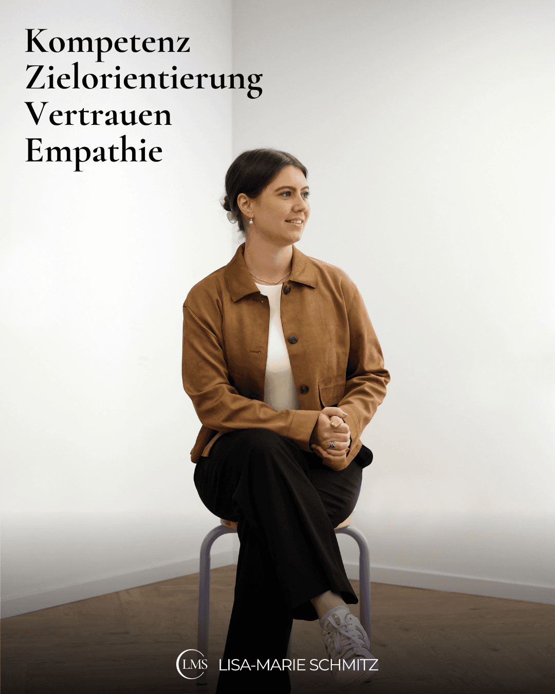Lisa-Marie sitzt in einem braunen Blazer auf einem Hocker mitten im Raum, schaut nach rechts, hat die Beine überschlagen, die Hände zusammengefallen und auf dem Bild stehen vier Wörter: Kompetenz, Zielorientierung, Vertrauen, Empathie.