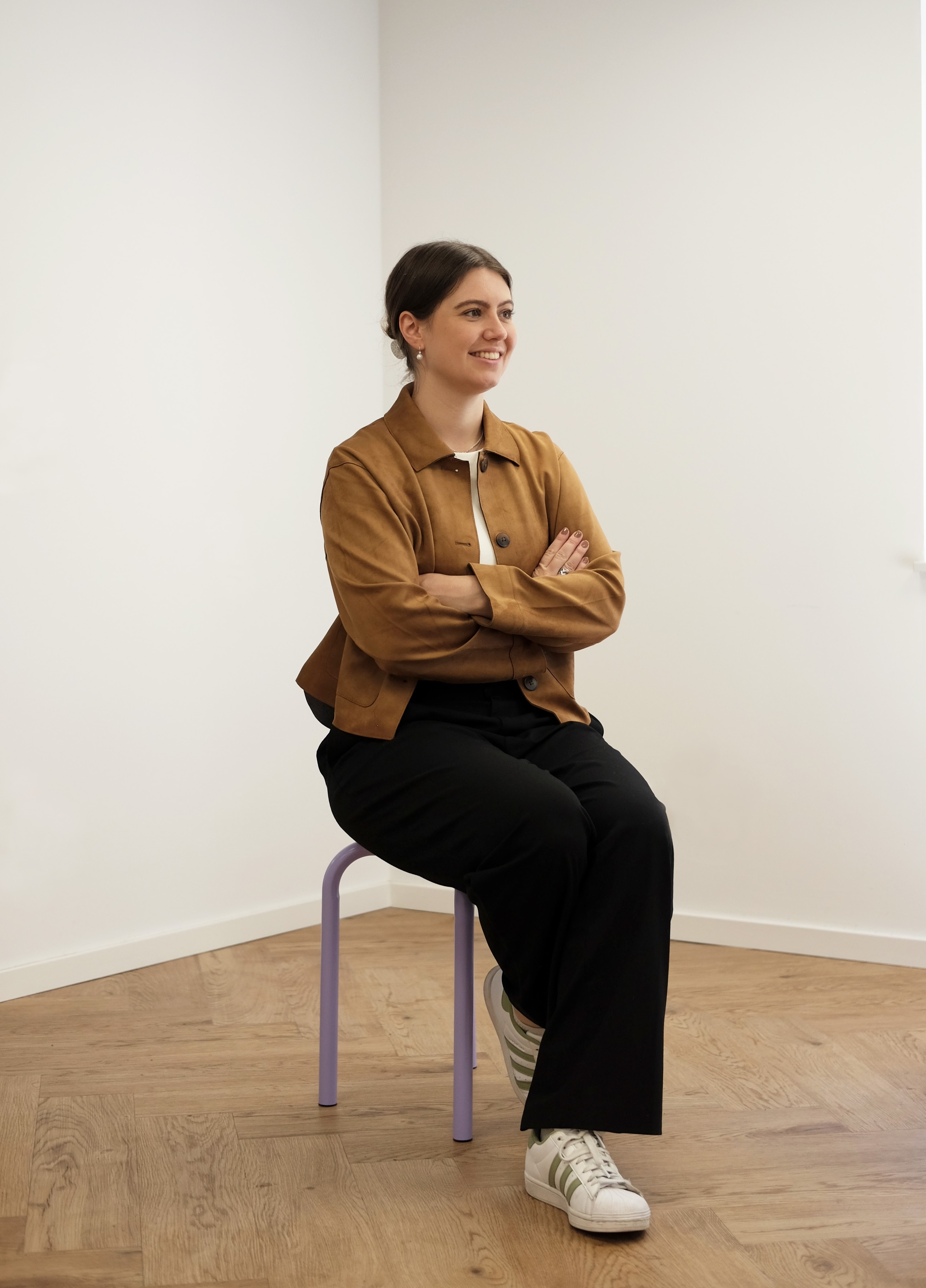 Lisa-Marie in brauner Jacke sitzt auf einem Stuhl, hat ihre Arme verschränkt und schaut in die Ferne