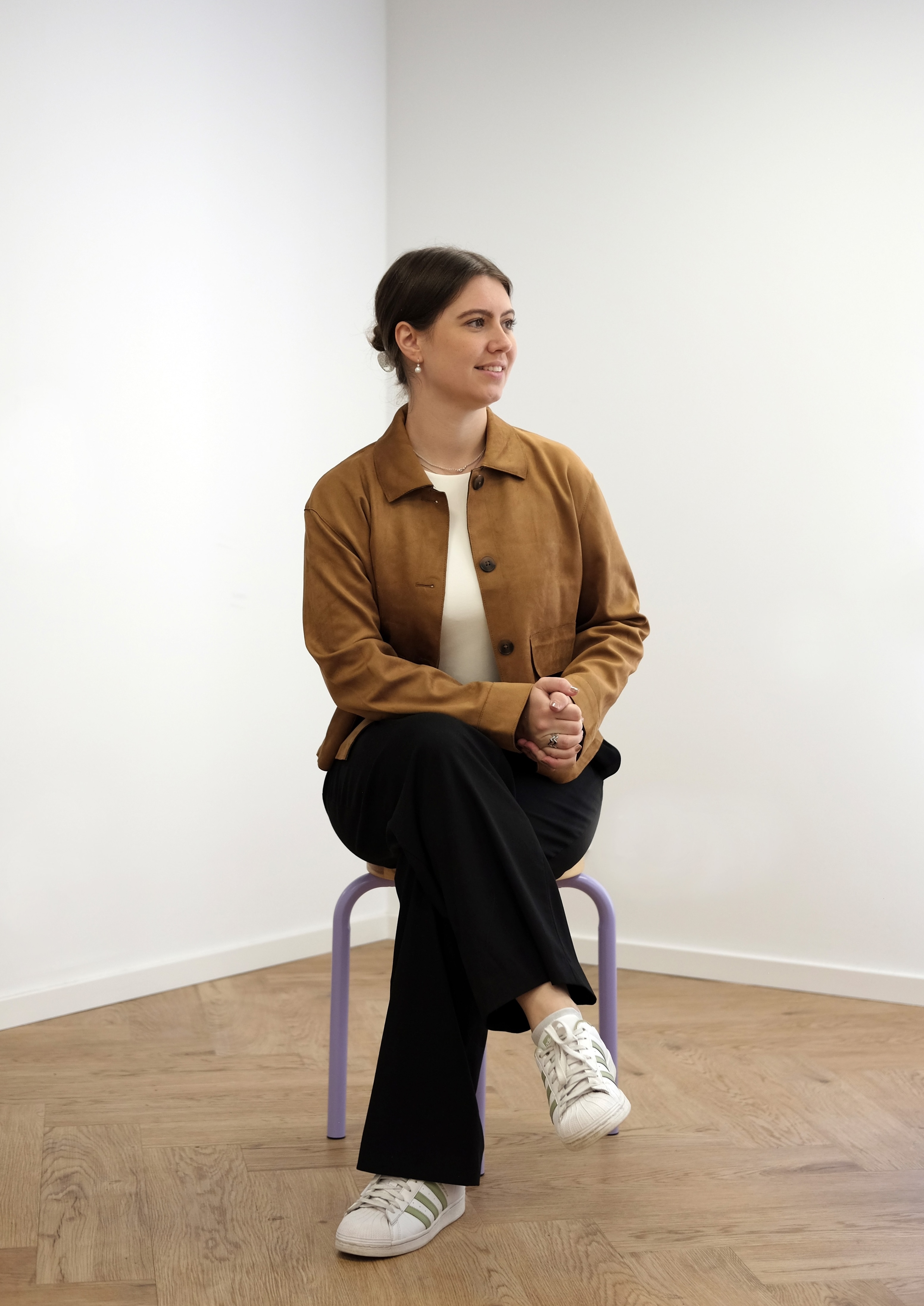 Lisa-Marie in brauner Jacke sitzt auf einem Stuhl, hat ihre Beine verschränkt und schaut in die Ferne